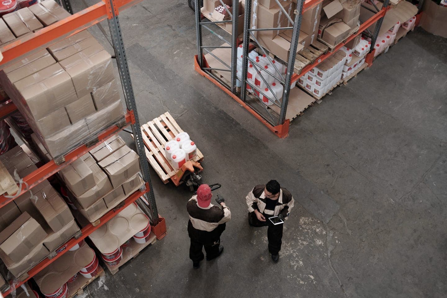 Warehouse aisle seen from above, with stocked shelves and two workers
